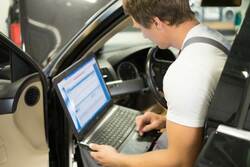 auto electrician diagnosing a car with a laptop and scan tool